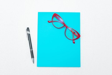 Pen and red women's glasses, blue notebook, white background, top view, copy space