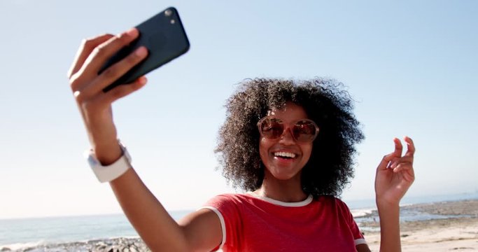 Woman taking selfie with mobile phone on beach in sunshine