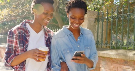 Twin sisters using mobile phone while walking in the city - Powered by Adobe