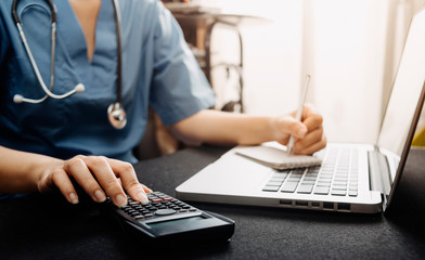 Healthcare costs and fees concept.Hand of smart doctor used a calculator and smartphone, tablet for medical costs at hospital in morning light