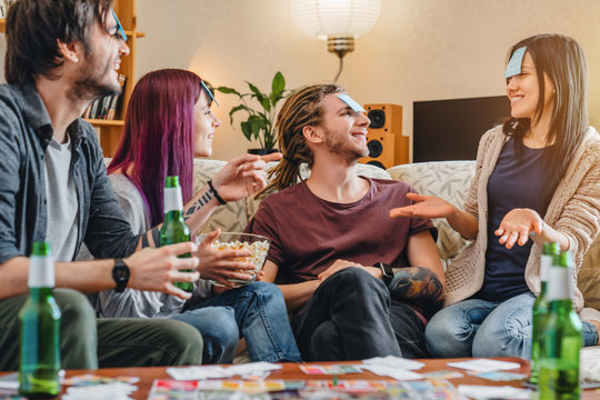 Group of friends with sticky notes playing name game with beer at home party