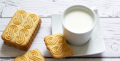 Cookies stacked and a cup of milk on a wooden background. Healthy snack.