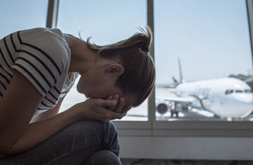Tired and stressed female traveler sitting at airport. Delayed flight, breakup concept. 