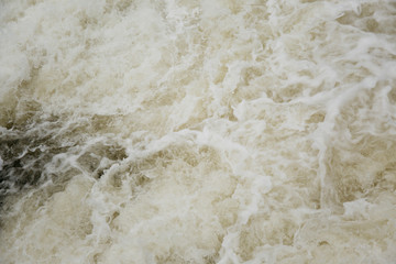 Fototapeta na wymiar Dirty yellow water with foam on a water-dam. Splashing rusty water