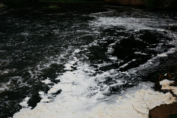 
Dirty yellow water with foam on a water-dam. Splashing rusty water