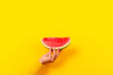 hand holds watermelon slice over yellow background.  Summertime concept.
