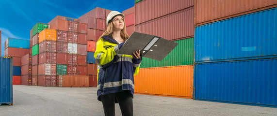 female docker with folder in protective gear in a container handling area