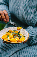 Pumpkin gnocchi with parmesan and sage. Plate in the hands of a woman in a sweater.