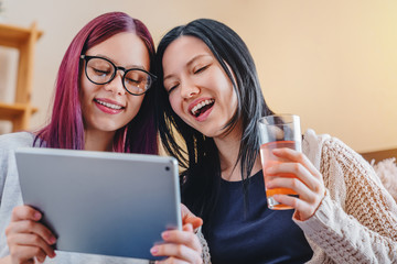 Close up of happy young female friends using digital tablet together on sofa at home