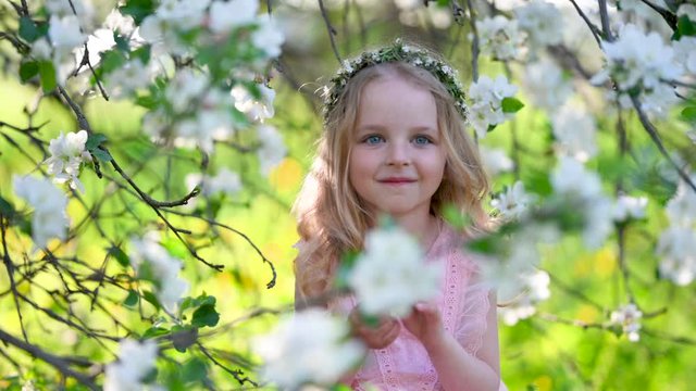 Portrait of a little cute girl in a flowered garden. A girl with white hair in a beautiful dress near the blooming branches of an apple tree. children, emotions.