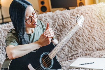 Young girl lighting marijuana joint while holding guitar at home