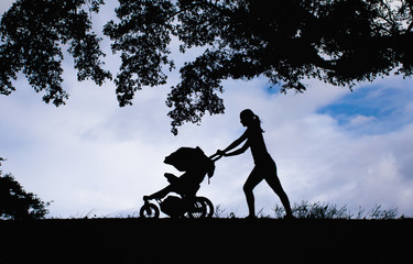 Mother pushing baby stroller through the park. 