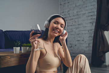 Joyful young woman drinking wine and listening to music