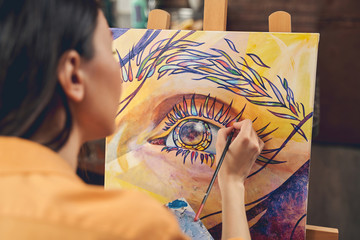 Young woman painting eye on easel in home art studio