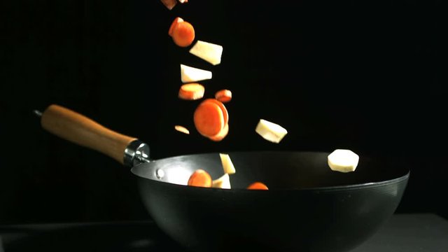 Chopped carrots and parsnips falling into a wok on black background