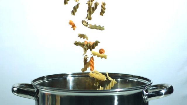 Tricolor fusilli falling into a saucepan