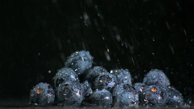 Water falling on blueberries on black background