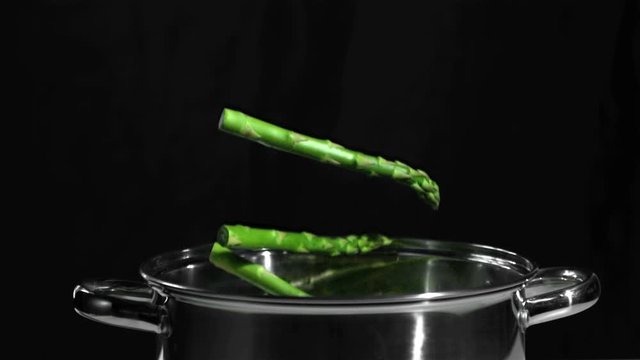 Asparagus falling in pot on black background