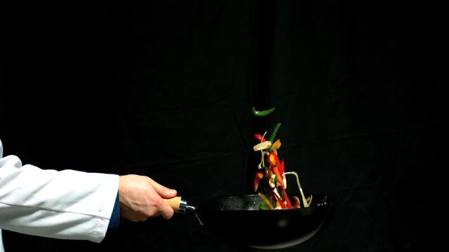Chef tossing vegetables in a wok black background