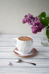 White coffee mug on a white wooden background with lilac blossom