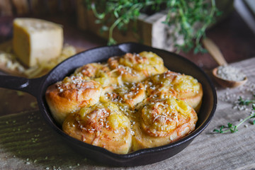 Savory cheese pastry with herbs and sesame seeds, round form on black pan, rustic wooden table with cheese, fresh thyme. Tasty snack - cheese rolls. Selective focus, copy space. Natural day light.