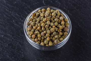 green peppercorns on dark slate stone background