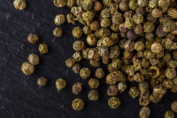 green peppercorns on dark slate stone background