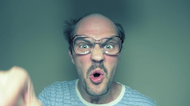 portrait. malicious bald mustachioed man with glasses swears looking at camera