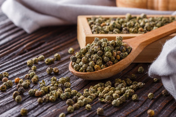 green peppercorns in wooden scoop on rustic background