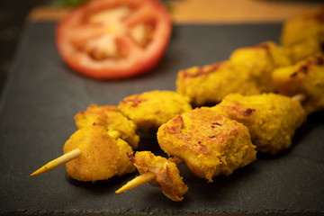 Moorish skewers on black stone and wooden cutting board with tomato slices