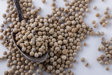 white peppercorns in spoon on white background