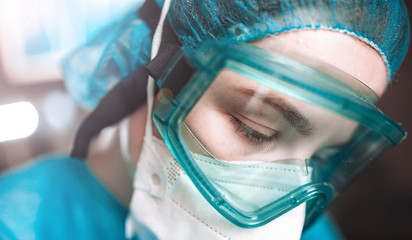 Female surgeon doctor in safety glasses and uniform in the operating room. Epidemiological medical worker.