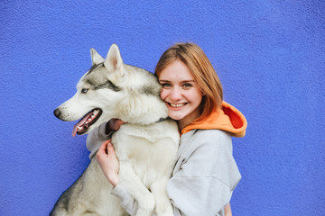 Isolated portrait of happy girl cuddle with her pet dog husky and smiling on blue background....