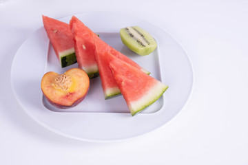 four slices of watermelon, peach and kiwi on a plate on a white background