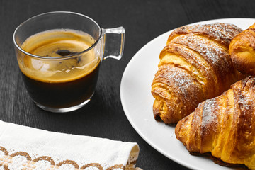 A cup of coffee, buttery croissants and cotton towel on a black background. Idea of breakfast. 