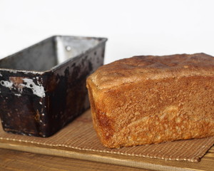 Freshly baked diet rye bread with a baking dish on a wooden table with a gray background.