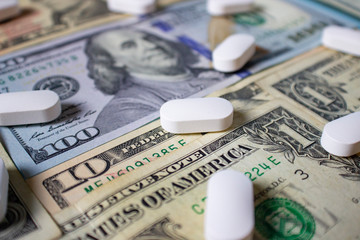 White pills in US dollars in denominations of one, ten and one hundred dollars. Health insurance concept.