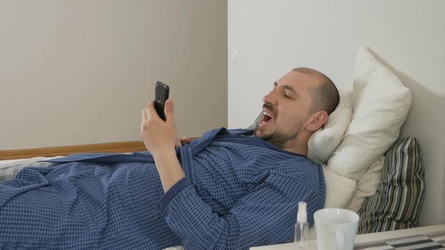 Lazy man using a mobile phone lying on a bed at home