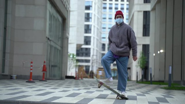 Young readhead hispter keeps skateboard on the soulder and walks the street looking to the camera. Outdoor. Cloudy. Protective mask. Portrait