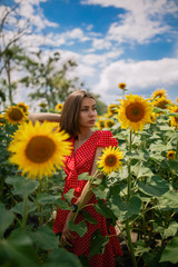 young beautiful caucasian girl in red dress in white dots stay in sunflower field 