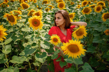 Obraz na płótnie Canvas young beautiful caucasian girl in red dress in white dots stay in sunflower field 