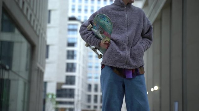 Young readhead hispter keeps skateboard on the soulder and walks the street looking to the camera. Outdoor. Cloudy. Protective mask. Portrait