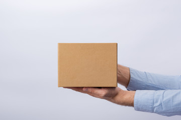 Man holding box at arm's length. White background. Square cardboard box. Delivery of parcels. Side view.
