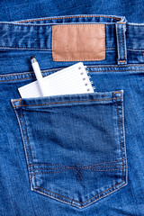 Close up of Jeans back pocket of classic blue denim pants with small notebook and a pen.