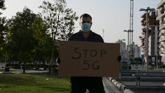 Man in medical mask and gloved hand hold a poster Stop 5G. Conspiratorial fake news about coronavirus and mobile communication concept