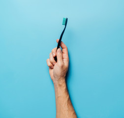 The concept of ecology and recycling or dentistry. A man's hand holds a black toothbrush on a blue background.