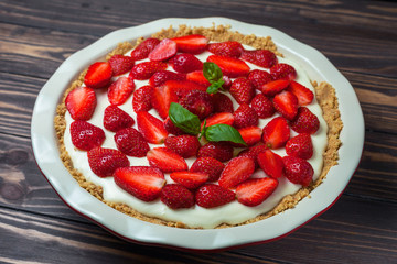 Strawberry cheesecake with basil leaves, in a red ceramic baking dish on a wooden background