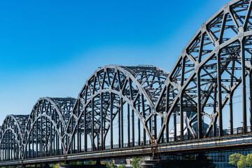 Large gray steel railway bridge against blue sky in sunny day. Riga, Latvia
