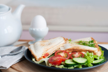 Hot sandwiches with cream cheese, cucumber, ham, tomatoes and peas sprouts on white plate. Breakfast with egg mist on white stand. 