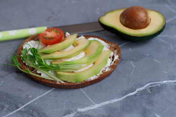 Vegetarian sandwich with cream cheese and avocado, tomatoes, peas sprouts  on dark gray background
